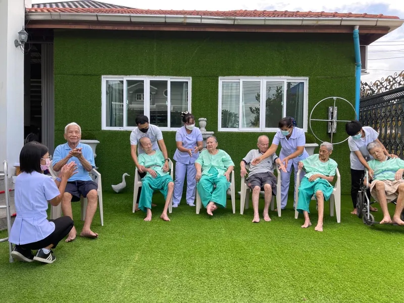 พยาบาลและผู้สูงอายุนั่งเก้าอี้หน้าอาคารสาขาปิ่นเกล้า
